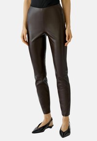 Bruine leren leggings met een strak pasvorm en een gladde textuur, met een hoge tailleband en een minimalistisch ontwerp. Gecombineerd met zwarte schoenen.