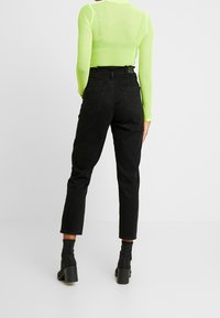 Zwarte hoog-waist jeans met een rechte pijp, gecombineerd met een doorzichtige neongroene top met lange mouwen. Zwarte enkellaarzen met hak maken de look compleet.