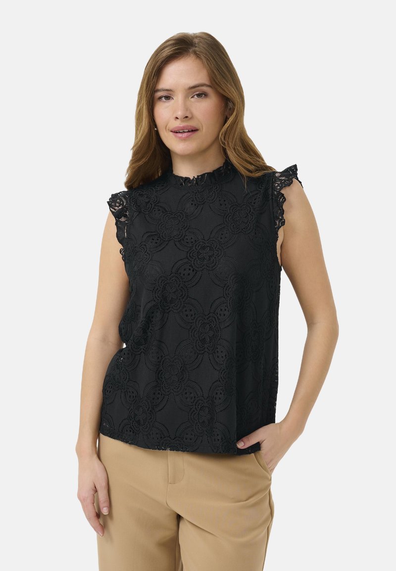 Črn brezrokavnik s čipkastim prelivom, cvetličnim vzorcem, nagubanimi rameni in visokim ovratnikom, v kombinaciji s bež hlačami.