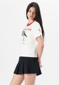 White t-shirt with red collar featuring a graphic design of a bird and text, paired with a black pleated skirt.