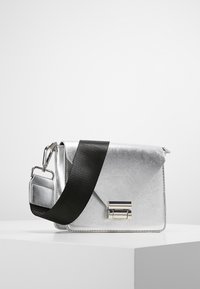 Stříbrná syntetická kabelka s elegantním trojúhelníkovým klopovým designem, vybavená černým textilním páskem a stříbrným kovovým zapínáním.