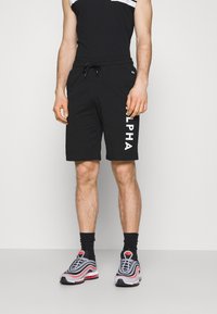 Svarta shorts med "ALPHA" tryckt i vitt på sidan, tillsammans med en svart ärmlös topp och flerfärgade träningsskor.