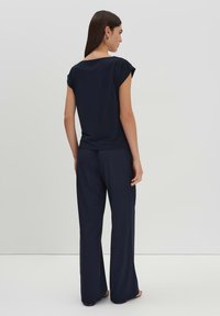 Top blu navy con maniche a cappotto e pantaloni blu navy a vestibilità ampia. Tessuto liscio con silhouette rilassata, indossato con sandali piatti.