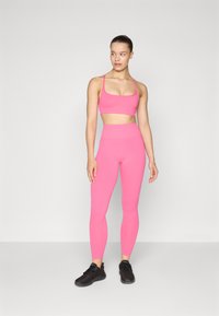 Reggiseno sportivo fucsia attillato e leggings a vita alta abbinati, realizzati in materiale liscio ed elastico. Indossato con scarpe da ginnastica nere.