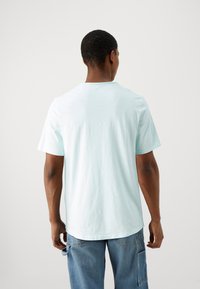 Camiseta de algodón de color azul claro, de mangas cortas, con escote redondo, corte recto, vista trasera, combinada con jeans de mezclilla azul que tienen bolsillos laterales.