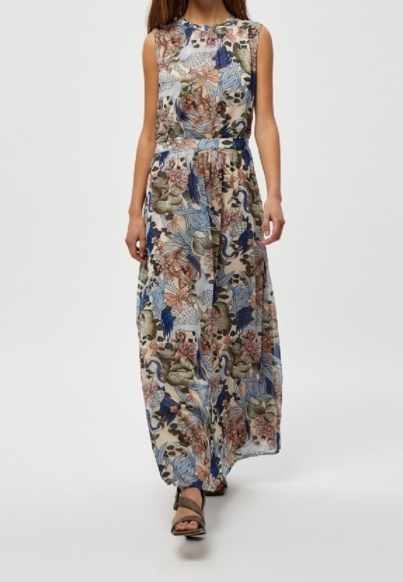 Femme portant une robe longue sans manches ceinturée avec des motifs floraux et feuillages colorés, associée à des sandales ouvertes marron.