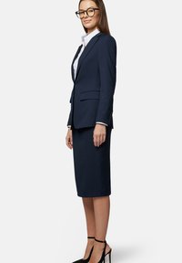 Navy elegancki garnitur z dopasowaną marynarką i spódnicą ołówkową do kolan. Teksturowana tkanina, w połączeniu z białą koszulą i czarnymi szpilkami.