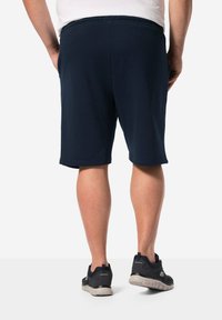 Pantaloni corti blu navy con vita elastica, che arrivano a metà coscia. Tessuto resistente con una superficie liscia. Scarpe sportive nere visibili.