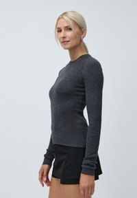 Harmaa ribattu pitkähihaiseen neuleeseen, jossa on pyöreä pääntie, tiukka malli ja pidennetyt hihansuut, yhdistetty mustiin shortseihin.