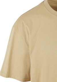 Μπεζ βαμβακερό κοντομάνικο T-shirt με στρογγυλή λαιμόκοψη και ορατές ραφές στον ώμο και στο μανίκι.