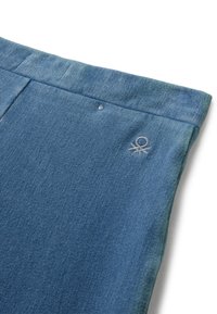 Primer plano de pantalones de mezclilla azul con cinturilla visible, costura del bolsillo y un pequeño logo bordado cerca de la cadera.