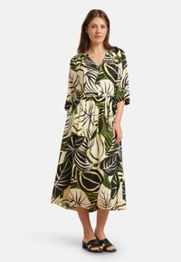 Blumenkleid aus leichtem Stoff, mit einer Mischung aus grünen, schwarzen und weißen Blattmustern, einem Bindegürtel in der Taille und Dreiviertelärmeln.