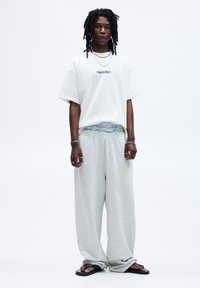 Oversized white t-shirt with blue embroidered text, paired with light gray wide-leg sweatpants and black flip-flops.