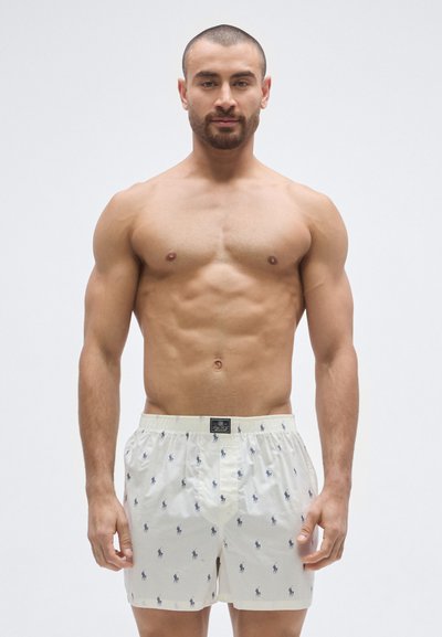 Pánske boxerky z ľahkej krémovej bavlny s opakujúcim sa vzorom malých tmavomodrých koní, elastickým pásom a štítkom s logom značky.