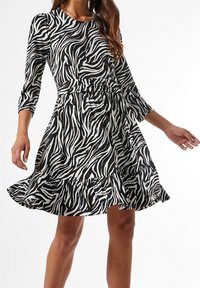 Vestido de estampado de cebra en blanco y negro con mangas de tres cuartos, cintura ajustada y dobladillo con volantes. Hecho de una tela ligera, presenta una falda acampanada.