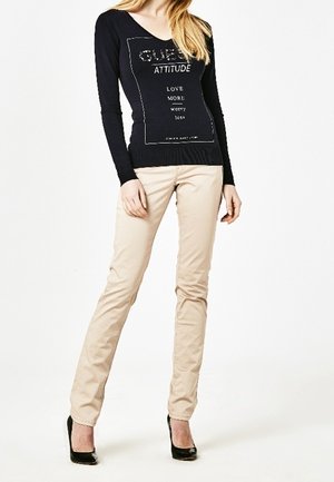 Navy long-sleeve shirt with printed text and cream fitted pants. Black high heels. Smooth texture; casual outfit.