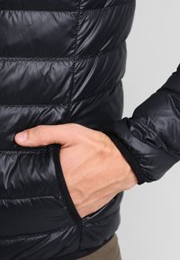 Zwarte donzen jas met een doorgestikt patroon, zijzak, en elastische manchetten voor een aansluitende pasvorm. Glad, glanzend materiaal met donkere accenten.