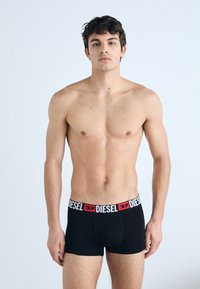Shorts de boxe noirs avec une ceinture logo « DIESEL » blanche et rouge. Le tissu semble lisse et ajusté contre le corps.