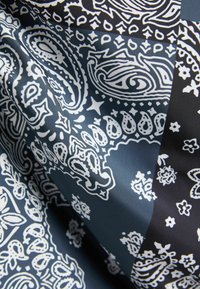 Tyg med vita paisleymönster på en mörkblå bakgrund, med intrikata mönster och en slät, glansig yta.