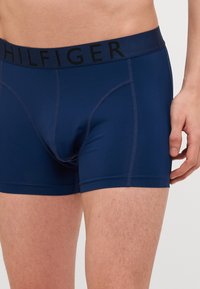 Boxer-briefs bleu marine en tissu extensible avec une ceinture noire portant le logo "HILFIGER", offrant une coupe ajustée et une texture lisse.