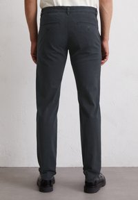 Dunkelgraue, maßgeschneiderte Hose mit glatter Textur, zwei Gesäßtaschen und geradem Bein. Getragen mit schwarzen Schuhen, minimalistischem Design.