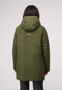 Groene geïsoleerde jas met een capuchon, met stiksels en een logo op de achterkant. Materiaal lijkt glad en waterafstotend.