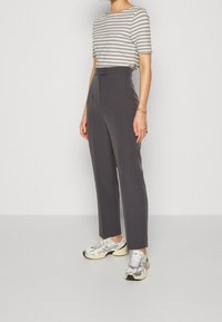 Pantalon gris sur mesure avec une texture lisse, taille haute et détail bouton, associé à un haut à manches courtes rayé et des baskets argentées.
