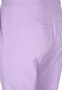 Närbild av lavendelfärgade byxor som visar bakfickor och en jämn tygstruktur.