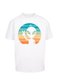 Weißes T-Shirt mit einem mehrfarbigen gestreiften Kreis, der eine weiße Alien-Silhouette zeigt, die vorne ein Friedenszeichen macht.