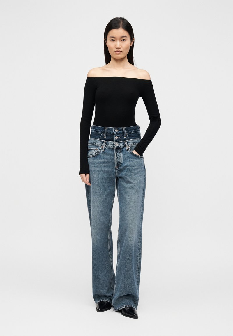 Haut noir épaules dénudées associé à un jean denim taille haute, jambe large, de couleur bleu clair, avec poches avant et boutons.