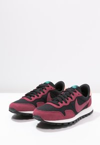 Ett par svarta och mörkröda Nike Air sneakers med detaljer i mesh och mocka, vita mellansulor, svarta yttersulor och en teal-färgad logotyp på tungan.