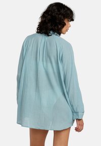 Himmelblaues Langarmshirt aus strukturiertem Stoff, mit lockerer Passform, abgerundetem Saum und geknöpften Manschetten, von hinten gezeigt.