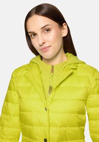 Żółta kurtka puchowa z przodem na guziki, wyposażona w kaptur i pikowaną teksturę. Solidny zamek błyskawiczny na wewnętrznej warstwie.