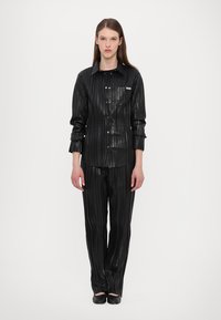 Fekete, redőzött ing és nadrág fényes anyagból, gombos elülső záródással, vízszintes texturált csíkkal és egy kis mellzsebbel.