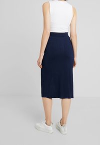 Marinblå ribbade midikjol med en åtsittande midja och mjuk textur, kombinerad med vita sneakers. Visningen visar baksidan av outfiten.