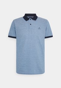 Světle modré polo tričko vyrobené z texturované látky s tmavě námořnickým límcem a manžetami, obsahující dva černé knoflíky a malé vyšívané logo.