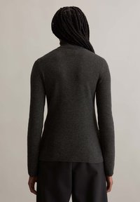 Dark gray ribbed sweater with a high collar and long sleeves, shown from the back, paired with dark trousers. Soft texture visible.