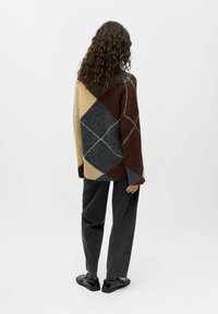 Oversized, knitted cardigan featuring a diamond pattern in brown, beige, dark gray, and light gray. Soft texture, wide sleeves, and open back.