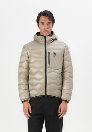 Beige gewatteerde jas met een capuchon, voorzien van golvende quiltsteken, ritssluiting en een ritsborstas met een logo. Zwarte accenten op de manchetten en de zoom.