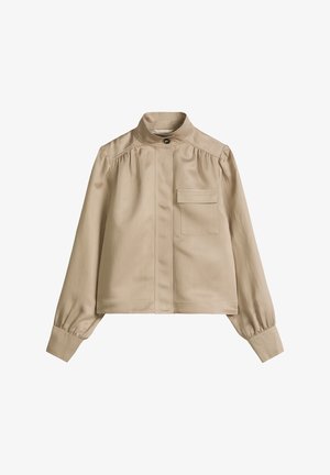 Veste longue beige à manches longues avec col montant, un bouton frontal unique, patte cachée, épaules froncées et une poche poitrine avec rabat.