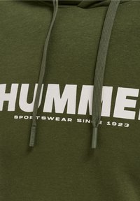 Sweat à capuche vert foncé avec texte blanc "HUMMER" et plus petit "SPORTSWEAR SINCE 1923" en dessous, avec cordons verts munis d’embouts en plastique.