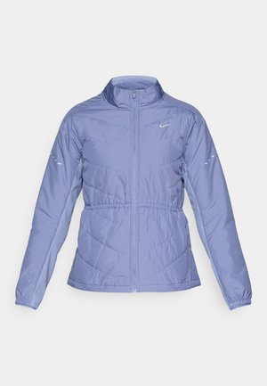 Cazadora deportiva de color púrpura claro con cremallera frontal, cuello alto, puños elásticos y patrón de rombos acolchado. Cuenta con un logo en el pecho.