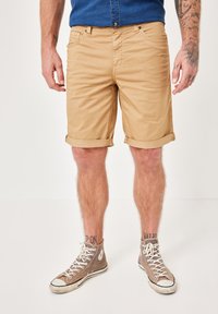 Beige cotton shorts with rolled hem, featuring front pockets and a button closure, paired with gray high-top sneakers.