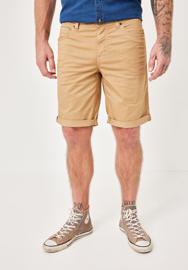 Beige cotton shorts with rolled hem, featuring front pockets and a button closure, paired with gray high-top sneakers.
