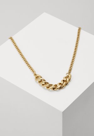 Collier chaîne en or épais avec des maillons alternant grands et petits, présenté sur une surface géométrique blanche.