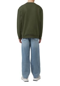 Oliwkowa bluza z okrągłym dekoltem, zestawiona z jasnoniebieskimi, szerokimi dżinsami o wyblakłej strukturze i tylnych kieszeniach.