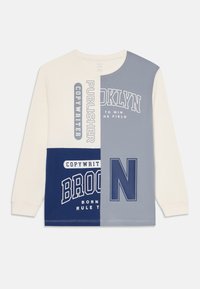 Langermet crewneck skjorte med kremfarge, blå og grå fargeblokker, med teksten "BROOKLYN," "PUBLISHER," og "COPYWRITER" trykt.
