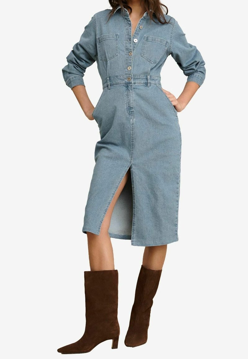 Abito camicia in denim blu chiaro con maniche lunghe, chiusura a bottoni sul davanti, due tasche sul petto e uno spacco frontale. Abbinato a stivali al ginocchio in suede marrone.