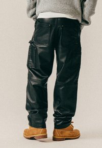 Sorte skinn cargo bukser med flere lommer, med en glatt tekstur og detaljer i gull. Kombinert med brune støvler.