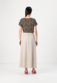 Top s leopardím vzorom s krátkymi rukávmi, skombinovaný s svetlo béžovou maxi sukňou a červenými sandálmi na podpätkoch, z pohľadu zozadu.